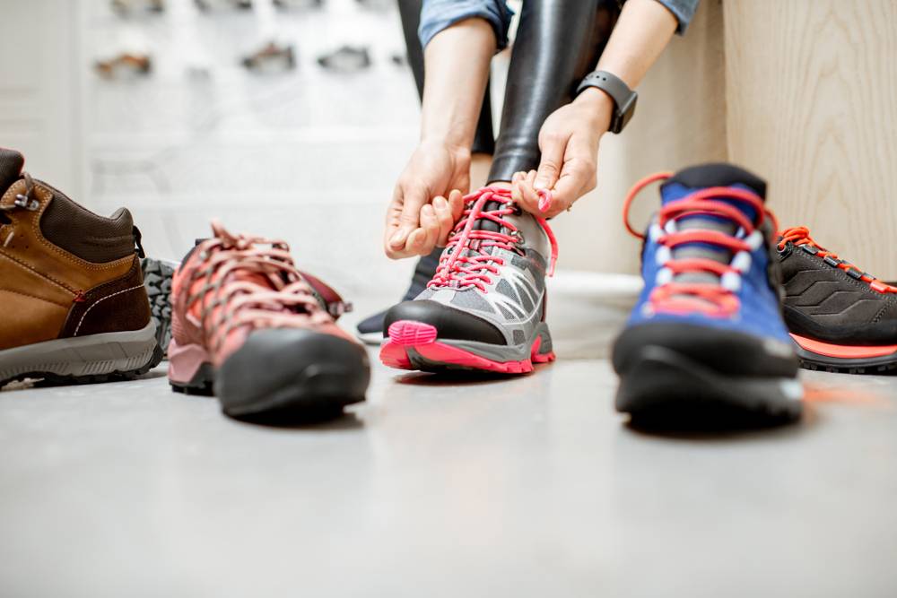 Ženska pomerja različno športno obutev in si zavezuje vezalke pohodnih čevljev.